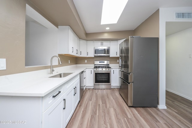 kitchen featuring visible vents, a skylight, a sink, appliances with stainless steel finishes, and light wood-type flooring