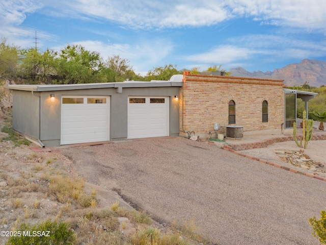 view of front of property featuring a garage, a mountain view, gravel driveway, and central AC