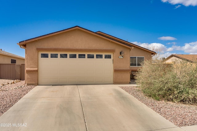 view of front facade with stucco siding, an attached garage, concrete driveway, and fence