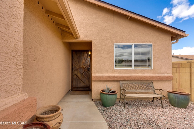 view of exterior entry featuring stucco siding and fence