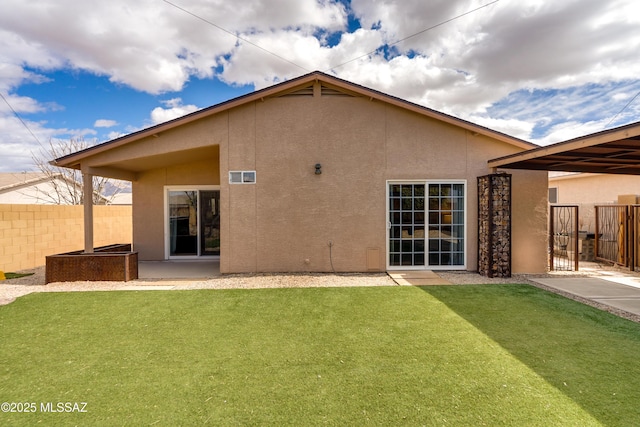 rear view of house with stucco siding, a yard, and fence