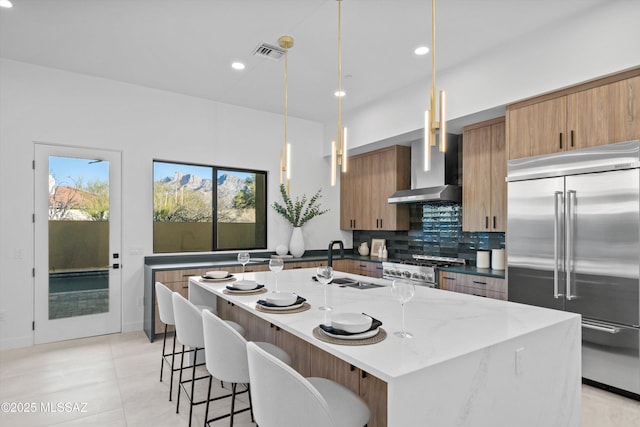 kitchen with backsplash, a breakfast bar area, high end appliances, wall chimney exhaust hood, and a sink