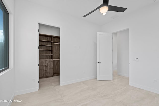 unfurnished bedroom with a walk in closet, baseboards, a closet, and ceiling fan