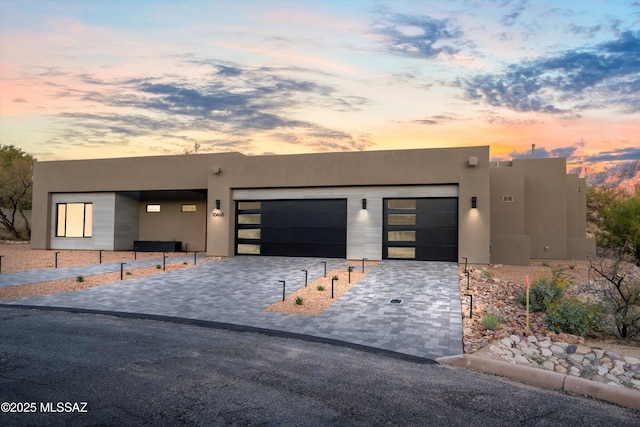 pueblo revival-style home featuring decorative driveway, a garage, and stucco siding