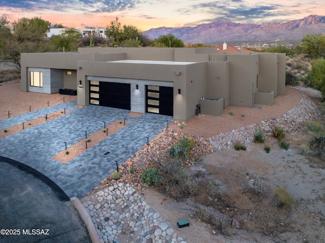 pueblo-style house with a garage, decorative driveway, a mountain view, and stucco siding