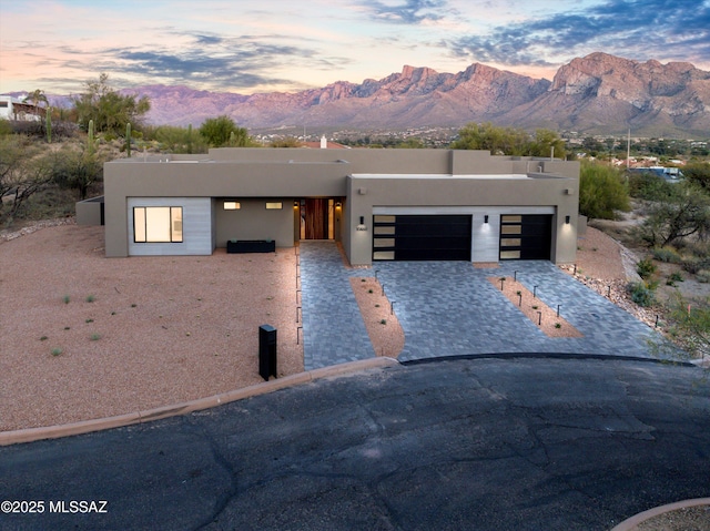 southwest-style home featuring a mountain view, stucco siding, an attached garage, and decorative driveway