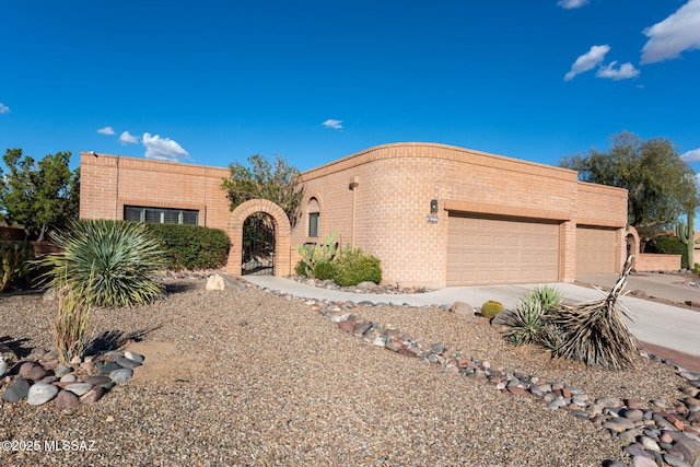 pueblo revival-style home with concrete driveway, a gate, a garage, and brick siding