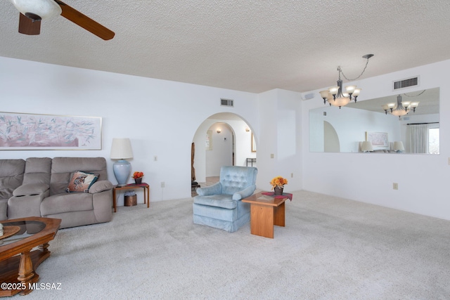 carpeted living room featuring visible vents, arched walkways, a textured ceiling, and ceiling fan with notable chandelier