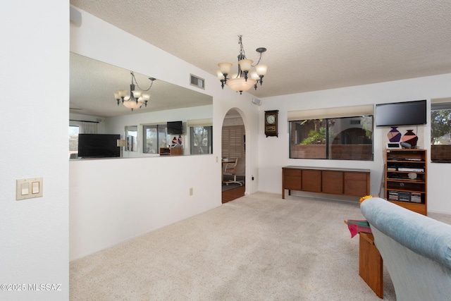 carpeted living room with a notable chandelier, arched walkways, visible vents, and a textured ceiling