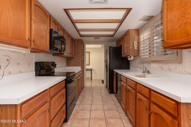 kitchen featuring brown cabinetry, black appliances, light countertops, and a sink