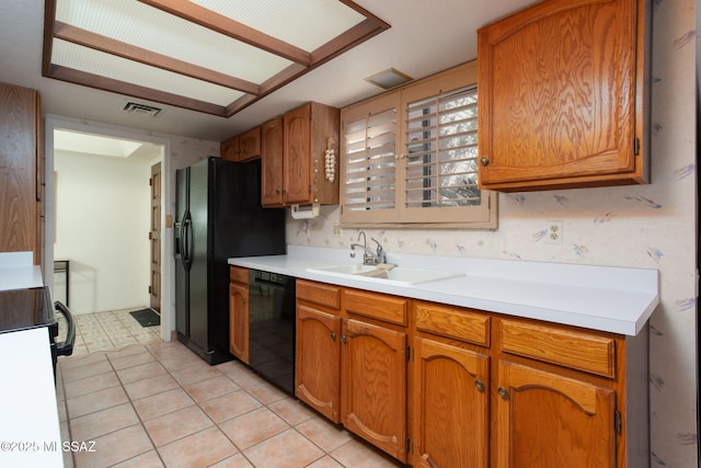 kitchen featuring visible vents, black appliances, a sink, brown cabinetry, and light countertops