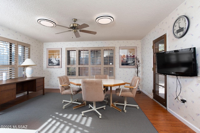 dining room with wood finished floors, baseboards, wallpapered walls, ceiling fan, and a textured ceiling