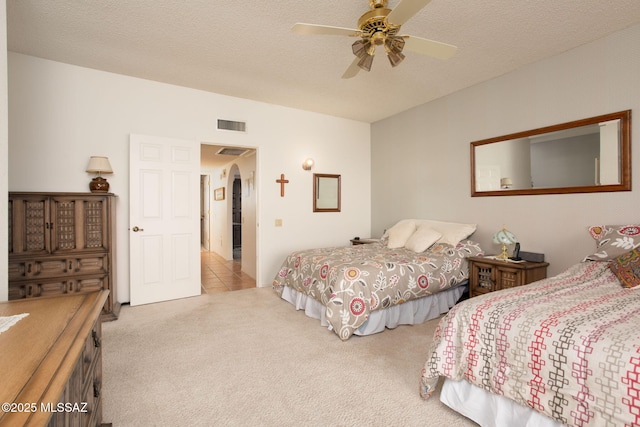 carpeted bedroom featuring ceiling fan, visible vents, arched walkways, and a textured ceiling