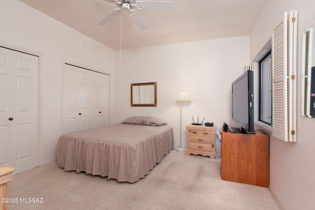 bedroom with carpet flooring, two closets, a textured ceiling, and a ceiling fan