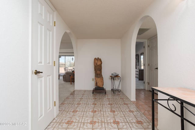 hall featuring arched walkways, light tile patterned floors, and a textured ceiling