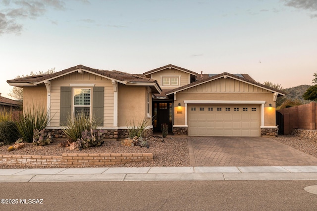 view of front of home featuring decorative driveway, an attached garage, fence, and stone siding