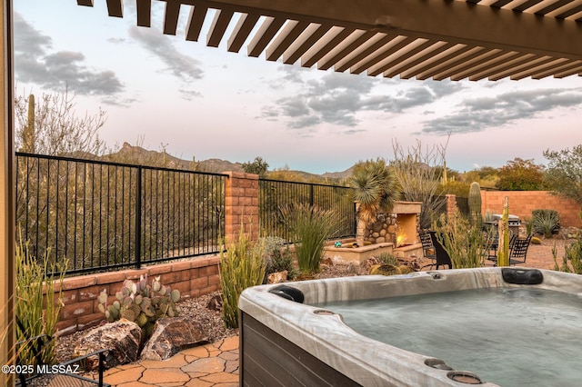 patio terrace at dusk featuring a fenced backyard, a mountain view, and a hot tub