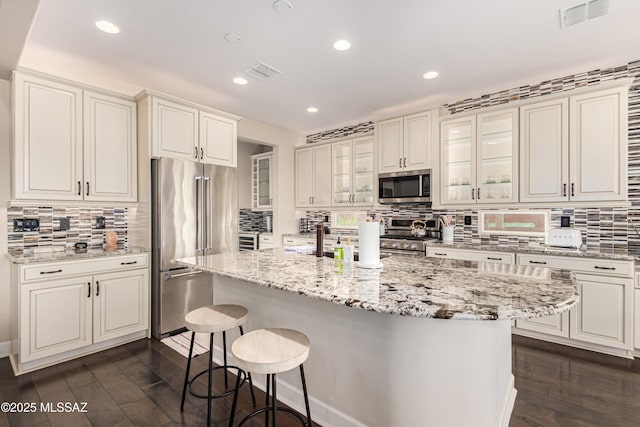 kitchen with premium appliances, visible vents, a breakfast bar area, and dark wood-style floors