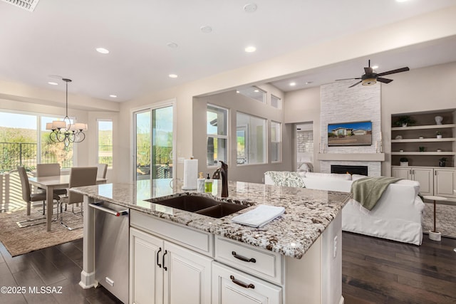 kitchen with an island with sink, a fireplace, dark wood-style flooring, a sink, and dishwasher