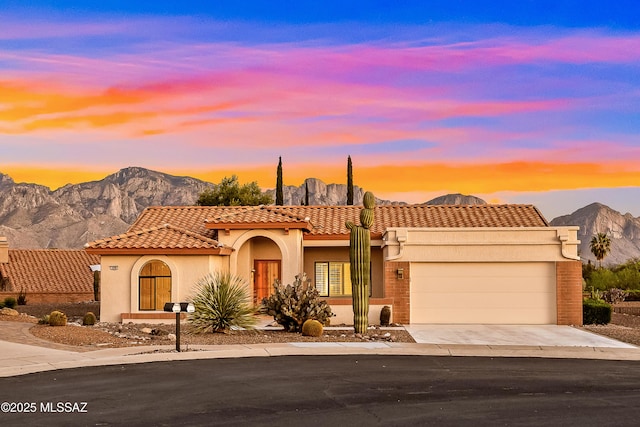 mediterranean / spanish home featuring an attached garage, a tiled roof, a mountain view, and stucco siding