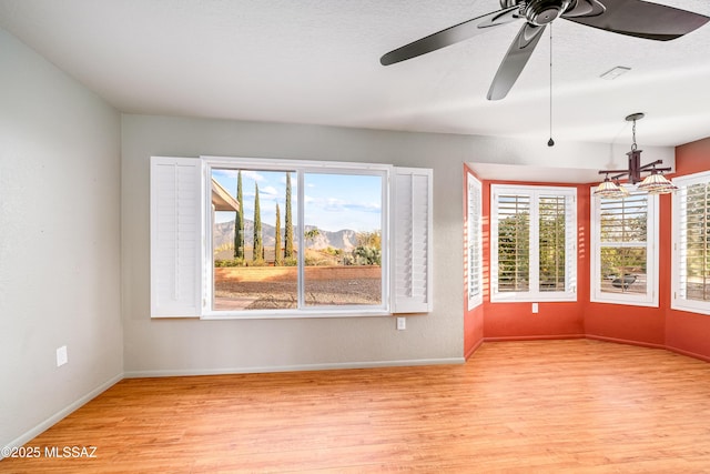 interior space featuring light wood-style floors, ceiling fan with notable chandelier, and baseboards