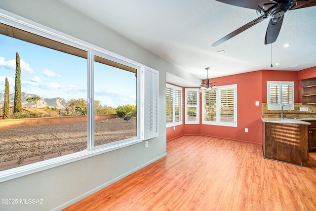 unfurnished living room with light wood-style floors, baseboards, and a ceiling fan