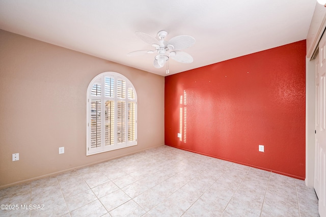 empty room featuring baseboards, a ceiling fan, and an accent wall