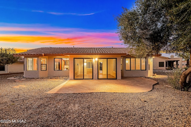 back of house at dusk featuring a patio area, stucco siding, and a tiled roof