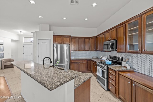 kitchen with tasteful backsplash, visible vents, glass insert cabinets, light stone counters, and stainless steel appliances