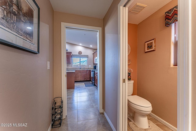 hall with a sink, visible vents, baseboards, and light tile patterned flooring