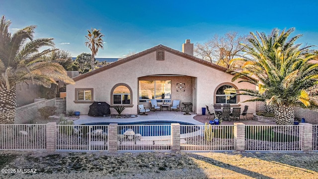 rear view of property featuring stucco siding, a chimney, a fenced backyard, a patio area, and an outdoor pool