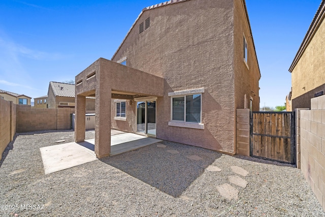 rear view of house featuring a fenced backyard, a gate, stucco siding, and a patio area