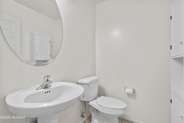 half bath with baseboards, toilet, and a sink