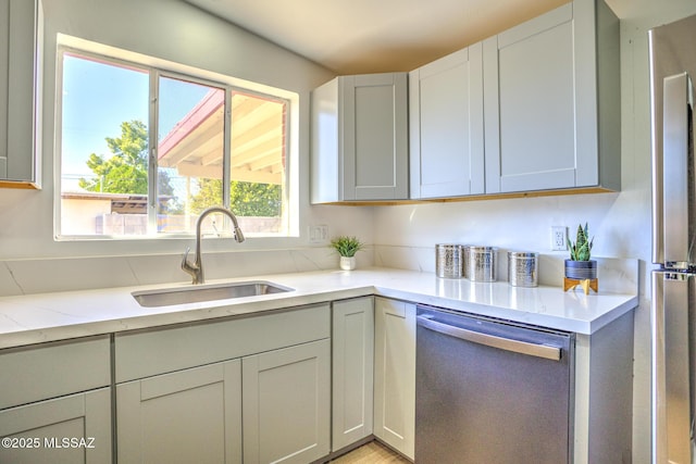 kitchen with light stone countertops, a sink, and dishwasher