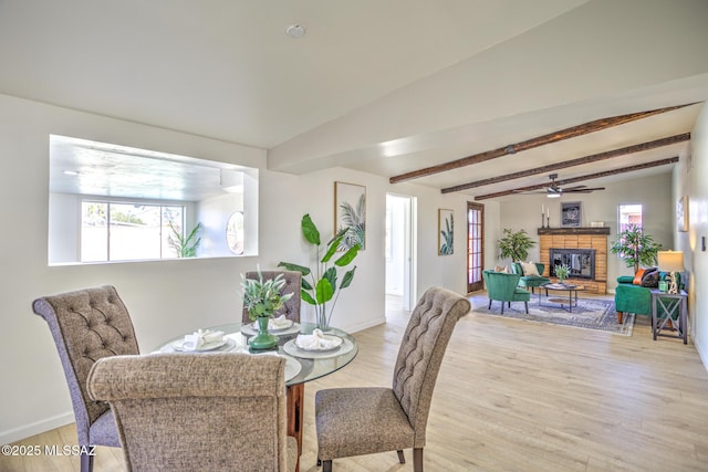dining area with a ceiling fan, a fireplace, light wood-type flooring, baseboards, and beamed ceiling