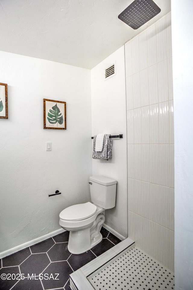 bathroom with toilet, tiled shower, visible vents, baseboards, and tile patterned flooring