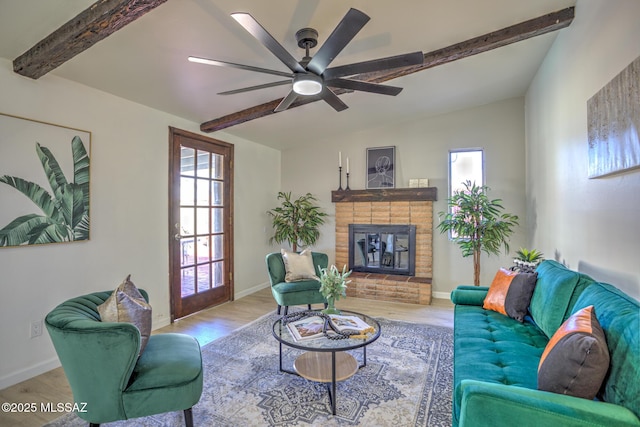 living area with lofted ceiling with beams, wood finished floors, a fireplace, ceiling fan, and baseboards