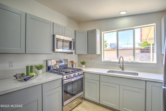 kitchen featuring a sink, light wood-type flooring, gray cabinets, and appliances with stainless steel finishes
