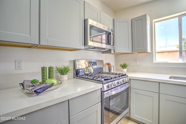 kitchen with gray cabinetry, light stone counters, and appliances with stainless steel finishes