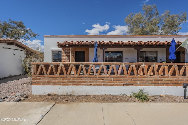 view of front of property with stucco siding, a tile roof, and fence