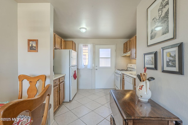 kitchen with brown cabinets, under cabinet range hood, white appliances, light countertops, and light tile patterned floors