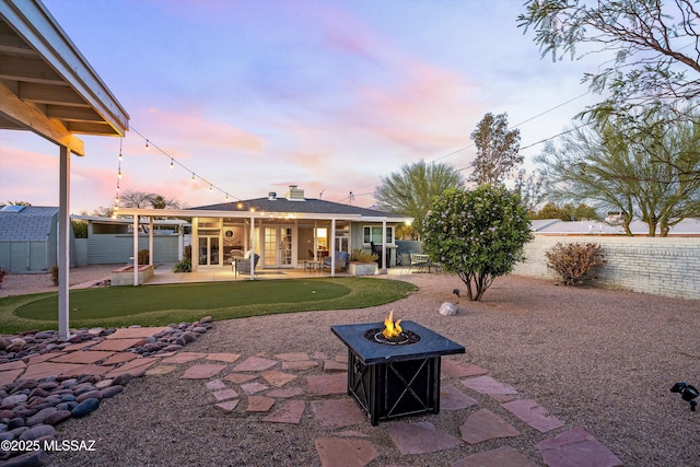 back of property at dusk with an outdoor fire pit, a fenced backyard, a chimney, french doors, and a patio area