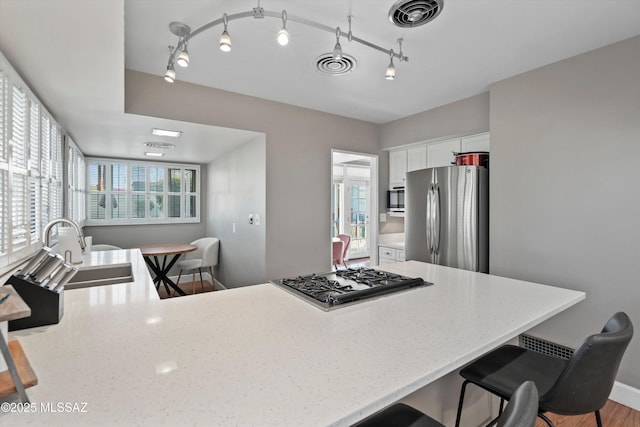 kitchen with visible vents, light stone counters, white cabinets, stainless steel appliances, and a sink