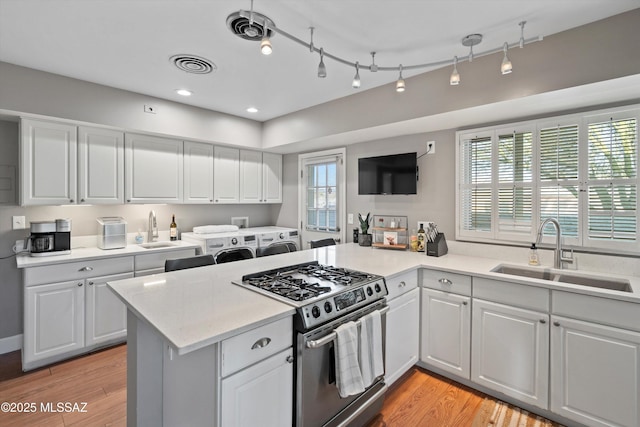 kitchen featuring visible vents, washing machine and dryer, stainless steel gas range, and a sink