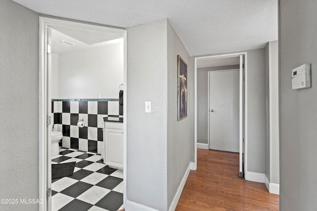 corridor featuring visible vents, a textured ceiling, baseboards, and wood finished floors