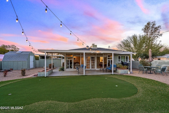 back of property at dusk featuring a storage unit, a patio, fence, french doors, and an outdoor structure