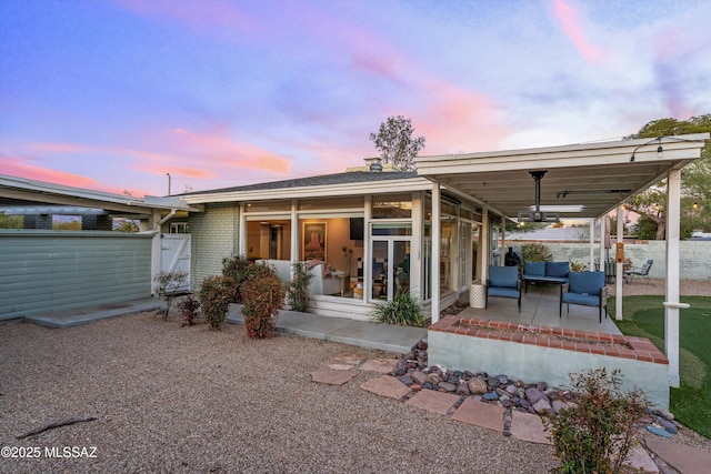 back of property at dusk with brick siding, a patio area, fence, and a sunroom