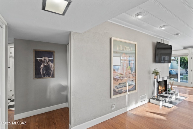 hall featuring visible vents, wood finished floors, baseboards, and a textured wall