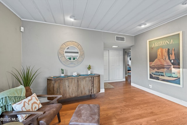 hall featuring baseboards, wood finished floors, visible vents, and ornamental molding