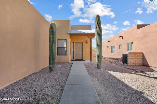 doorway to property with central air condition unit, stucco siding, and metal roof